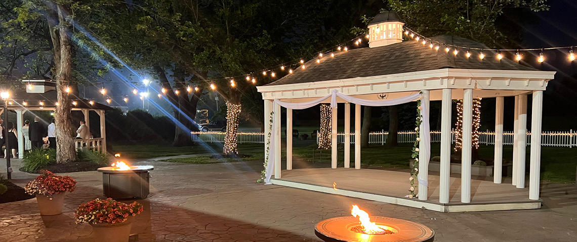 Patio gazebo at night lit up with patio string lights and fir pits