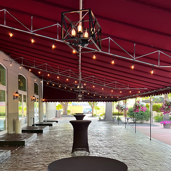 Red awning over the patio with string lights and high top tables