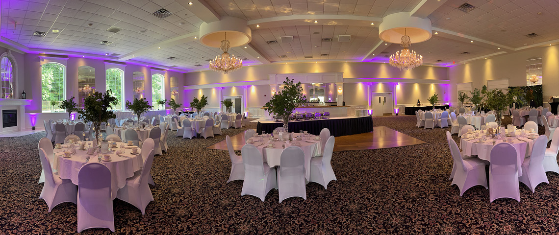 Large banquet hall with chandeliers, purple lighting and tall green centerpieces
