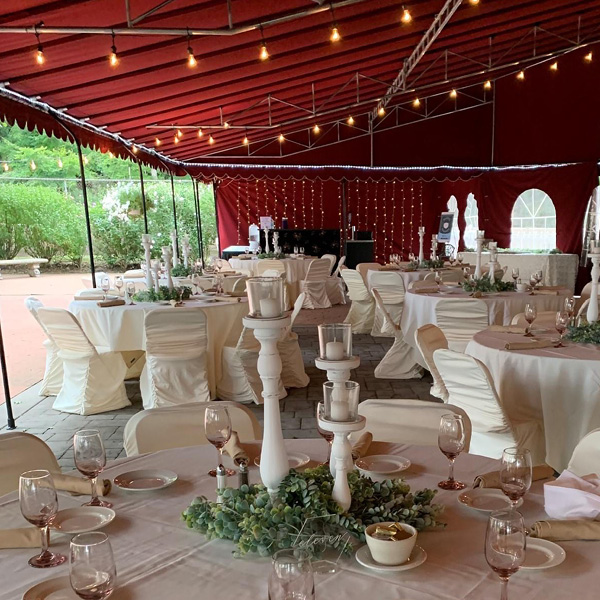 Covered patio space with a red awning and tables with white linens and greenery
